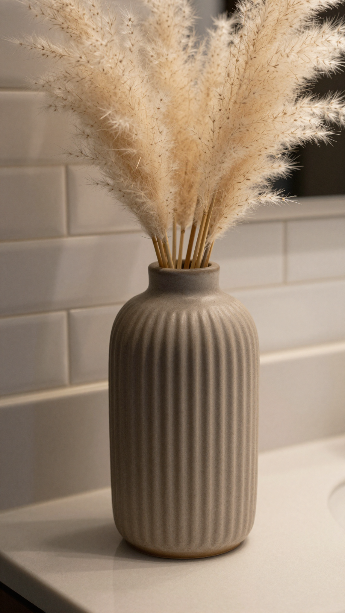 Textured ceramic vase with ribbed design holding dried pampas grass on a bathroom counter